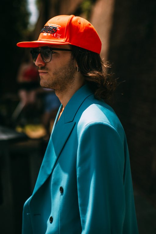 Man with orange cap and turquoise blazer in sunlight during Pitti Immagine