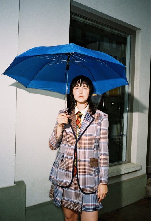 Frau in kariertem Sakko mit blauem Schirm.