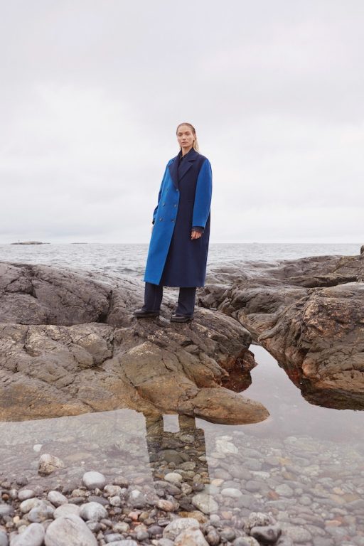Model in blau-schwarzem Mantel steht auf Felsen am Meer in House of Dagmar.