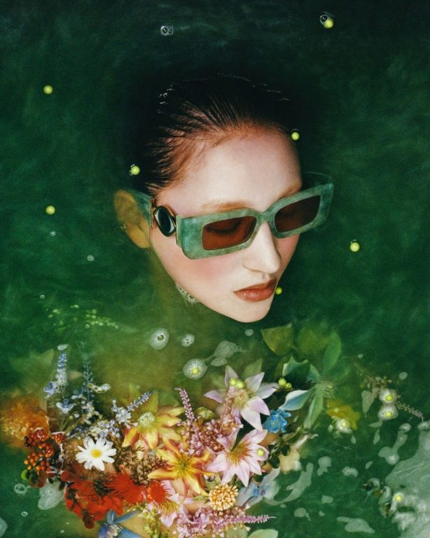 Mit Blumen geschmücktes Model, die eine grüne Sonnenbrille trägt.