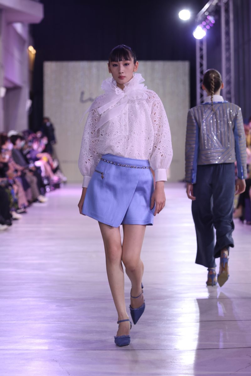 Model in hellblauem Minirock und weißer, gerüschter Bluse auf dem Laufsteg